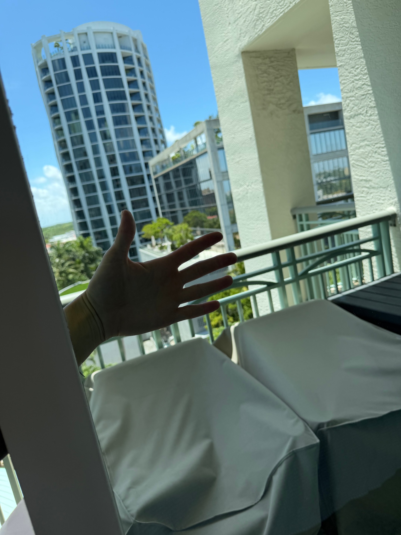 Hand on a crystal-clear balcony glass door with a Miami view after cleaning